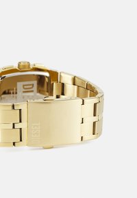 Goldfarbene Edelstahl-Armbanduhr mit rechteckigem Zifferblatt, gebürsteter Oberfläche und Klappverschluss; mit dem eingravierten Schriftzug "DIESEL" auf dem Verschluss.