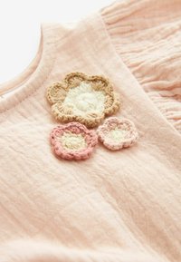 Jasnoróżowa tkanina z trzema haftowanymi kwiatami w odcieniach beżu, kremu i delikatnego różu. Faktura jest lekko pomarszczona, co dodaje wizualnego zainteresowania.