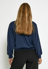 Navy blue, long-sleeve sweatshirt with a relaxed fit, ribbed cuffs, and a V-shaped back design. Soft fabric with a smooth texture.