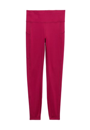 Kvinde iført en magenta tætsiddende kortærmet top og leggings, stående med det ene ben løftet, hvide sneakers og stribede sokker på en lys baggrund.