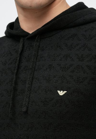 Camisola preta com capuz feita de tecido de malha texturizado, apresentando um padrão subtil e um pequeno logótipo dourado bordado no peito.