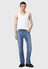 Czysty biały top na ramiączkach w połączeniu z jasnoniebieskimi, postarzałymi dżinsami o prostym kroju i subtelnym wyblaknięciu. Czarnłe buty o teksturowanym wykończeniu.