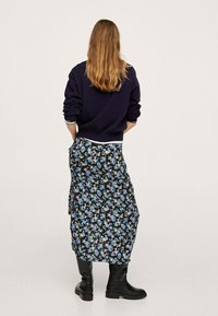 Gonna lunga floreale nera con motivi blu e rosa, abbinata a un pullover blu navy. Il materiale sembra morbido; presenta una vestibilità rilassata e una fessura laterale.