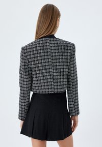 Mustat ja valkoiset ruutukuosiset cropped-takit, valmistettu teksturoidusta kankaasta, yhdistetty mustiin plissertuihin hameisiin. Yksinkertainen, räätälöity siluetti.