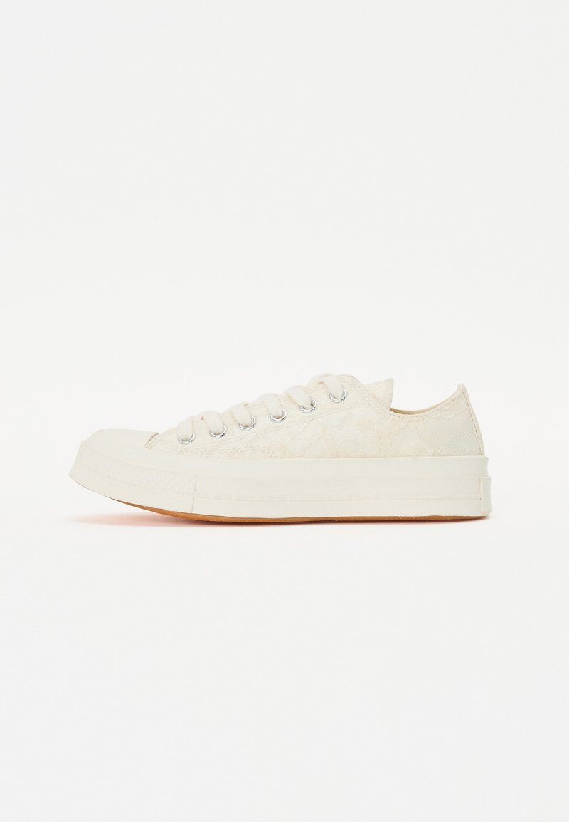 Krémszínű vászon tornacipő texturált fűzős mintával, hat szemlyukral, kerek orral és gumi talppal.