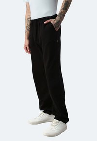 Schwarze Jogginghosen mit elastischem Bund und Kordelzug, seitlichen Taschen und slim-fit Schnitt. Kombiniert mit weißen Sneakers.