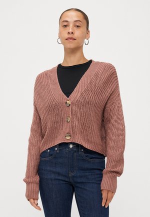 Cardigã cropped de malha em rosa envelhecido com decote em V, três botões de madeira e punhos canelados, combinado com jeans de denim azul escuro.