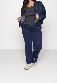 Mörkblå vida byxor, kombinerade med en mörk denimjacka och en marinblå topp med vita prickar och knappdetaljer, fulländar looken.