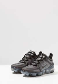 Scarpe da athletic nere con tomaia in rete e suola in gomma. Presentano un design snello, accenti testurizzati e unità di ammortizzazione ad aria visibili.