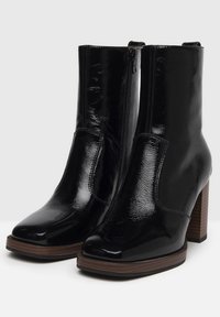 Bottines en cuir verni noir avec une finition brillante, un talon bloc et une fermeture éclair sur le côté ; texture lisse et silhouette simple.