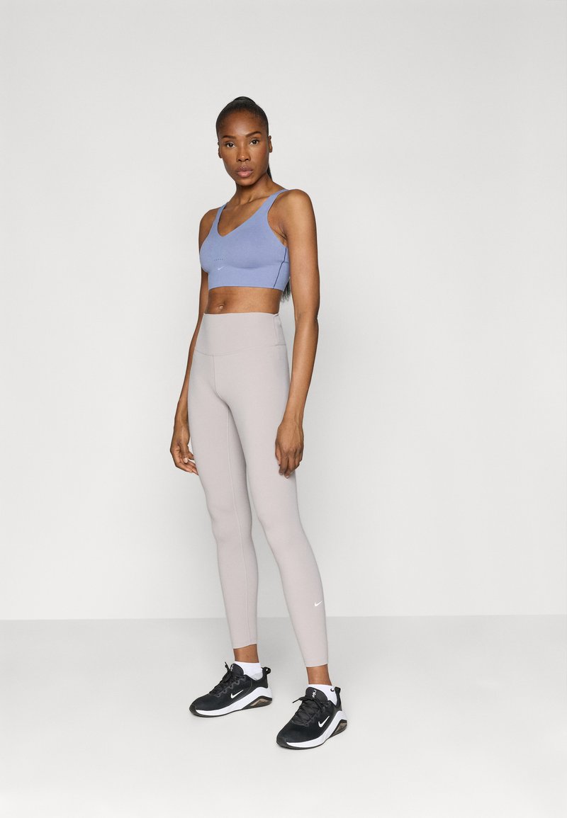 Light blue sports bra, beige high-waisted leggings, and black sneakers with white accents, against a plain gray background.