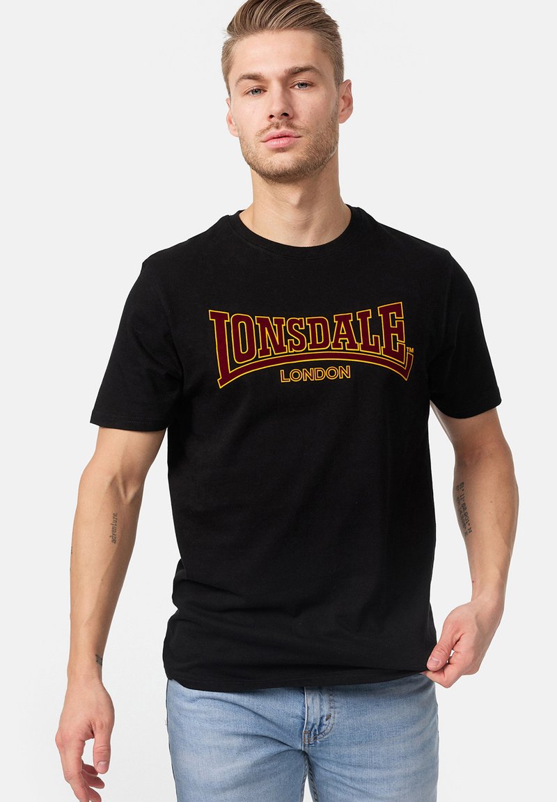 Tricou negru din bumbac cu guler rotund, având un grafic îndrăzneț în roșu și galben "LONSDALE LONDON" pe piept. Mâneci scurte.