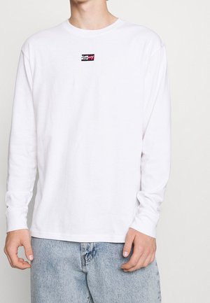 T-shirt blanc à manches longues en coton, avec un petit patch logo multicolore sur la poitrine et un col rond.
