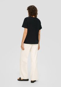 Zwarte katoenen t-shirt met korte mouwen, gezien vanuit de rug, gecombineerd met off-white wijde broek en zwarte platform sandalen.