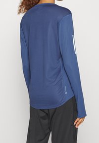 Langärmliges Sportoberteil in Marineblau mit strukturiertem Muster, rundem Ausschnitt und Logodetail am unteren Saum.