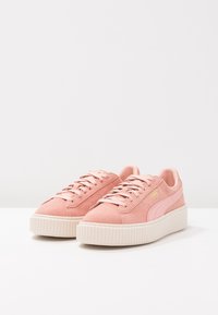 Une paire de baskets à plateforme en daim rose avec de épais semelles beiges et des lacets assortis sur une surface blanche.