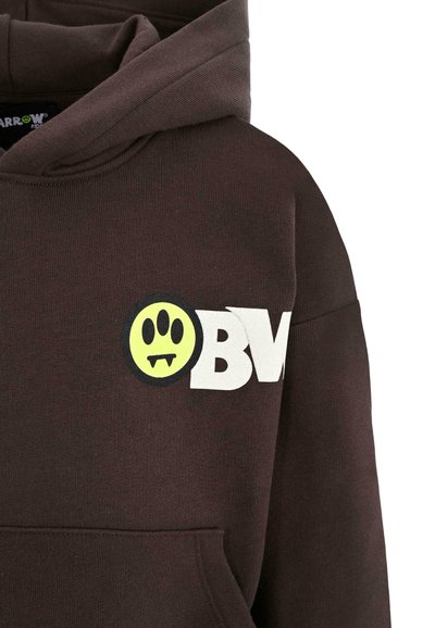 Bruine hoodie met een gele glimlachende gezichtlogo met tanden en witte tekst "BV." Bevat een voorzak en een gestructureerde stof.