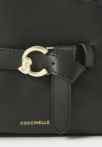 Borsa a tracolla nera in pelle con una fibbia in metallo dorato, dettagli cuciti e il nome del brand "Coccinelle" impresso nella parte inferiore.