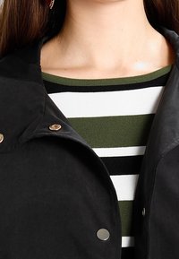 Black jacket with snap fasteners over a striped green and white top. The jacket has a smooth texture and a structured collar.