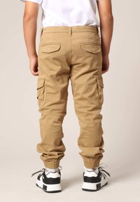 Khaki cargobroeken met elastische boorden, platte achterzakken en zijvakken, gecombineerd met zwart-witte sneakers.