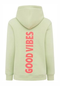 Haut à capuche vert menthe avec cordon de serrage, présentant un grand texte "GOOD VIBES" en rose fluo verticalement dans le dos. Texture douce, coupe décontractée.