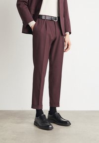 Burgundy tailored trousers with pleats, cuffed hem, paired with black leather shoes and a black belt, worn over a light sweater.