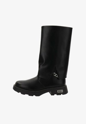 Bota negra de caña alta, hecha de material sintético suave, con suela gruesa y acentos metálicos decorativos en el lateral. Presenta una puntera redondeada.