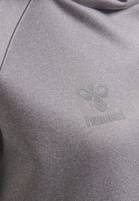 Felpa grigia con una texture morbida, caratterizzata da un design del logo tono su tono al centro. Il materiale sembra elastico e comodo.