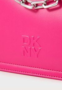 Τσάντα χειρός από ψεύτικο δέρμα σε έντονο ροζ χρώμα με ανάγλυφο λογότυπο "DKNY", ασημένια αλυσίδα και ραφές κατά μήκος της άκρης.