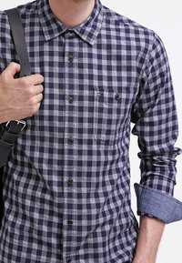 Marineblauw en grijs geblokt shirt met lange mouwen, button-down kraag en een borstzak. Voorzien van bruine knopen en denimaccenten op de manchetten.