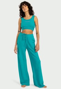 Turkis crop tank top med rund halsudskæring parret med vidde-sweatpants, der har elastisk talje og snor. Blød stoftekstur.
