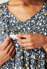 Blommig klänning i mörkblått med korta ärmar och V-ringning. Har en rynkad midja och en dold öppning för enkel åtkomst.