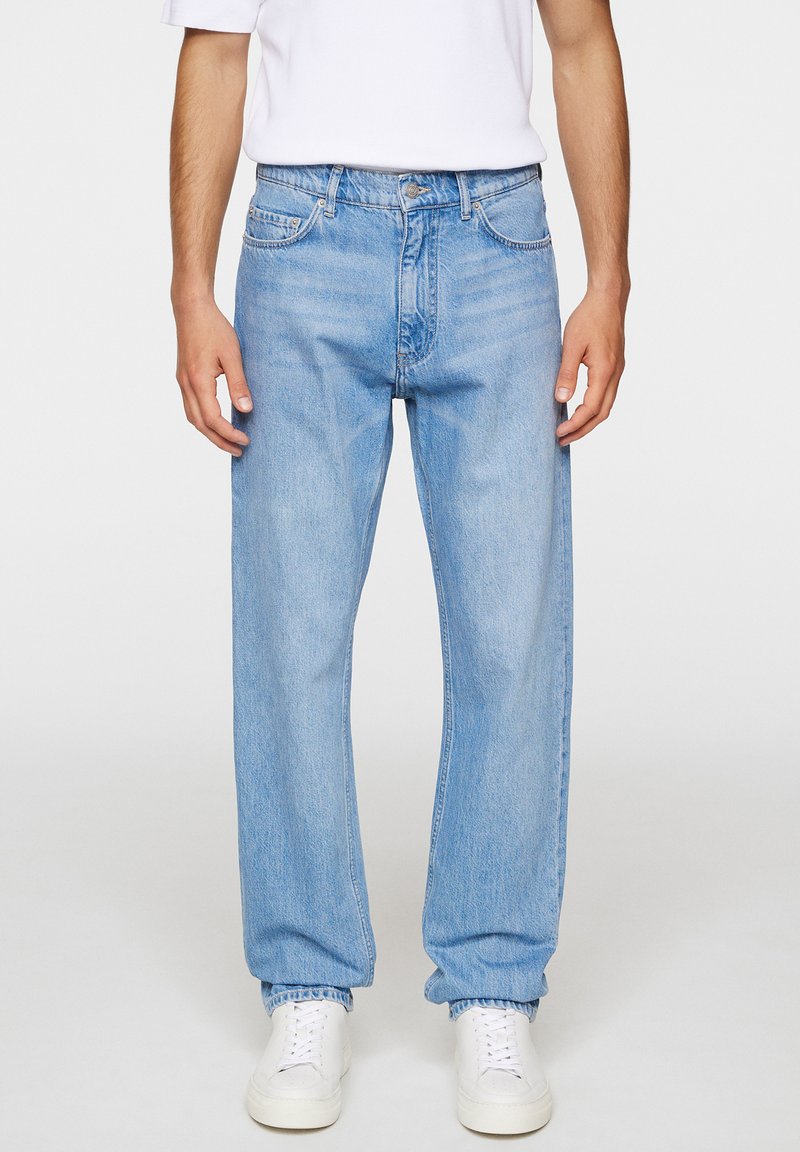 Ljusblå denimjeans med avslappnad passform, featuring fem fickor och elastiska muddar, i kombination med vita sneakers.