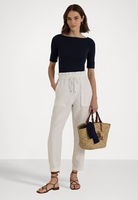 Navy fitted top, white linen joggers with elastic waistband and front pockets, brown strappy sandals, and a woven basket bag with a blue accent.