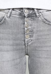 Jeans de mezclilla gris de cintura alta, con cinco botones de metal en la bragueta y un ligero desvanecimiento en toda la tela.