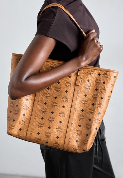 Brown leather tote bag with embossed black logos, diamond patterns, and a smooth texture. Features two sturdy handles for carrying.