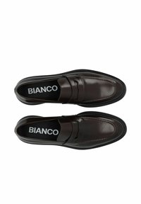 Mocassins en cuir marron avec une texture lisse, bout arrondi, coutures visibles et une semelle intérieure marquée. Semelle en caoutchouc noire fine.