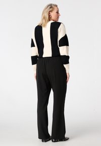 Pull rayé noir et crème avec tissu texturé, associé à un pantalon noir taille haute et des chaussures plates noires cloutées.