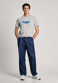 Siva pamučna majica s plavim logotipom "Pepe Jeans London", u kombinaciji sa širokim tamnoplavim trapericama i bijelim tenisicama.