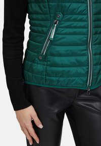 Grön puffväst med quiltat mönster, två sidofickor med dragkedja och svarta ribbade tröjärm. Kombinerad med stilrena svarta läderbyxor.