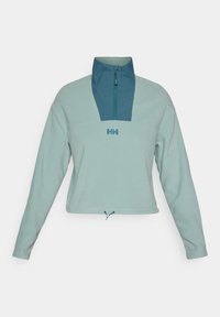 Polo de forro polar en un suave tono verde azulado con cuello de media cremallera en navy, cuenta con un logo frontal, dobladillo ajustable y mangas largas. Textura suave.