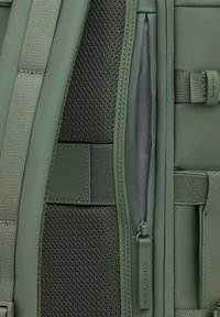 Grüner Rucksack aus strukturiertem Stoff, mit glatten, matten Elementen und einer Reißverschlusstasche. Verfügt über Tragegurte und eine Akzentuierung mit dem Markennamen.