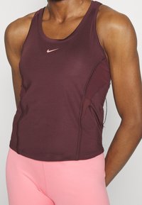 Canotta sportiva bordeaux con logo rosa, caratterizzata da un design aderente, scollo rotondo e pannelli laterali strutturati. Abbinata a pantaloni rosa chiaro.