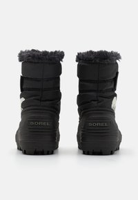 Botas de invierno impermeables negras con cuello de piel sintética, tejido acolchado y suela de goma. Presenta una etiqueta de marca prominente y una suela con textura para mayor tracción.