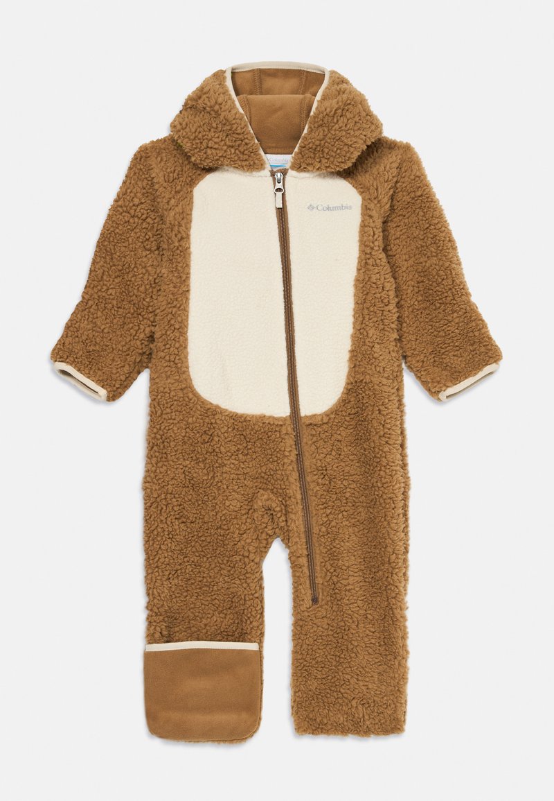 Combinaison en sherpa marron avec une patch crème, fermée par une fermeture éclair, capuche et poignets élastiques. Texture douce avec un détail en tan contrasté au niveau des pieds.