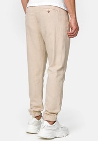Joggers en lin beige avec des poignets élastiques, une poche arrière avec bouton et des poches latérales, associés à des chaussures de sport blanches.