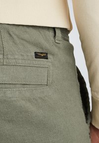 Pantalones verde oliva con tela texturizada, que cuentan con un bolsillo trasero y una etiqueta negra y dorada titulada "American Classic".