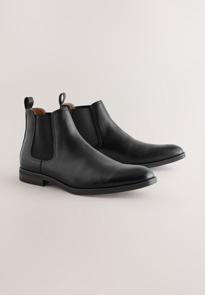 Stivaletti Chelsea neri in pelle con pannelli elastici ai lati, texture liscia, punta appuntita e linguette di presa; dotati di un tacco basso in legno.