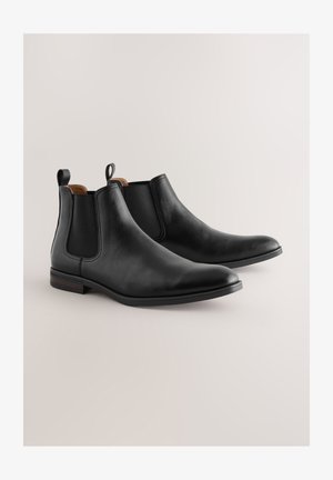 Botas Chelsea de cuero negro con paneles elásticos en los laterales, textura lisa, punta estrecha y tiradores; con un tacón bajo de madera.