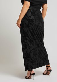 Svart maxikjol med blommönster, mjuk textur, figurnära midja och sidoklyvning. Kombinerad med svarta högklackade sandaler.